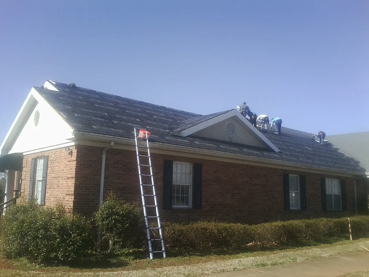 Crew tearing shingles off a brick ranch roof with a ladder set — Emergency Roof Repair work by our crew in Irvine